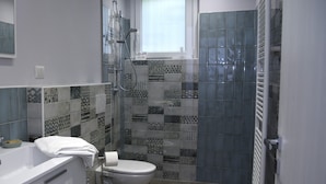 Une salle de bain moderne équipée d’une douche, de toilettes et d’un bidet. Elle est agrémentée de carreaux décoratifs et possède une fenêtre située au-dessus de la douche.