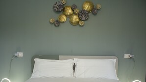 Un lit avec du linge de lit blanc, une couvre-lit à motifs et une composition décorative fixée au mur, composée d’objets circulaires et sphériques.