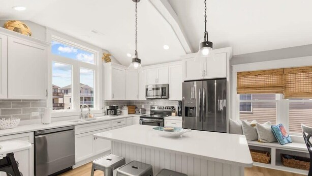 A modern kitchen with white cabinetry, stainless steel appliances, and a large island with bar stools. - Sojourn's Chipwrecked | 2Min Walk to Beach, Bikes (Kill Devil Hills)