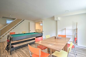 Una habitación con mesa de billar, una mesa de madera con sillas y una escalera.