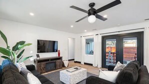 A modern living room with a flat-screen TV, dark sofas, a coffee table, and a ceiling fan. - BEAUTIFULLY Remodeled Home, Close to Downtown!! (Paso Robles)