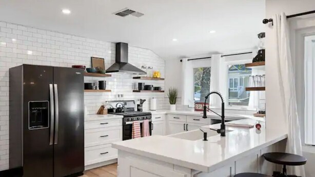 A modern kitchen with white cabinetry, a stainless steel refrigerator, a central island with stools, and a window with a view of the outside. - BEAUTIFULLY Remodeled Home, Close to Downtown!! (Paso Robles)