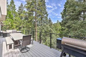 Een terras met een tafel, stoelen, een barbecue en uitzicht op hoge bomen.