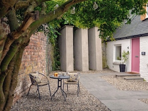 Un patio con muro de ladrillo, estructura de concreto, una puerta rosa y dos sillas de mimbre con una mesa.