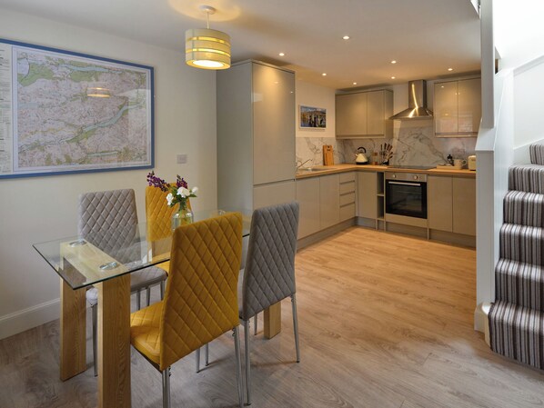Una cocina moderna con horno empotrado, una zona de comedor con mesa y sillas de vidrio, y un mapa en la pared.