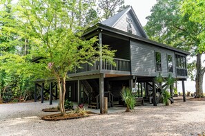 Une maison à deux étages avec un balcon, entourée d’arbres et donnant sur une allée gravillonnée.