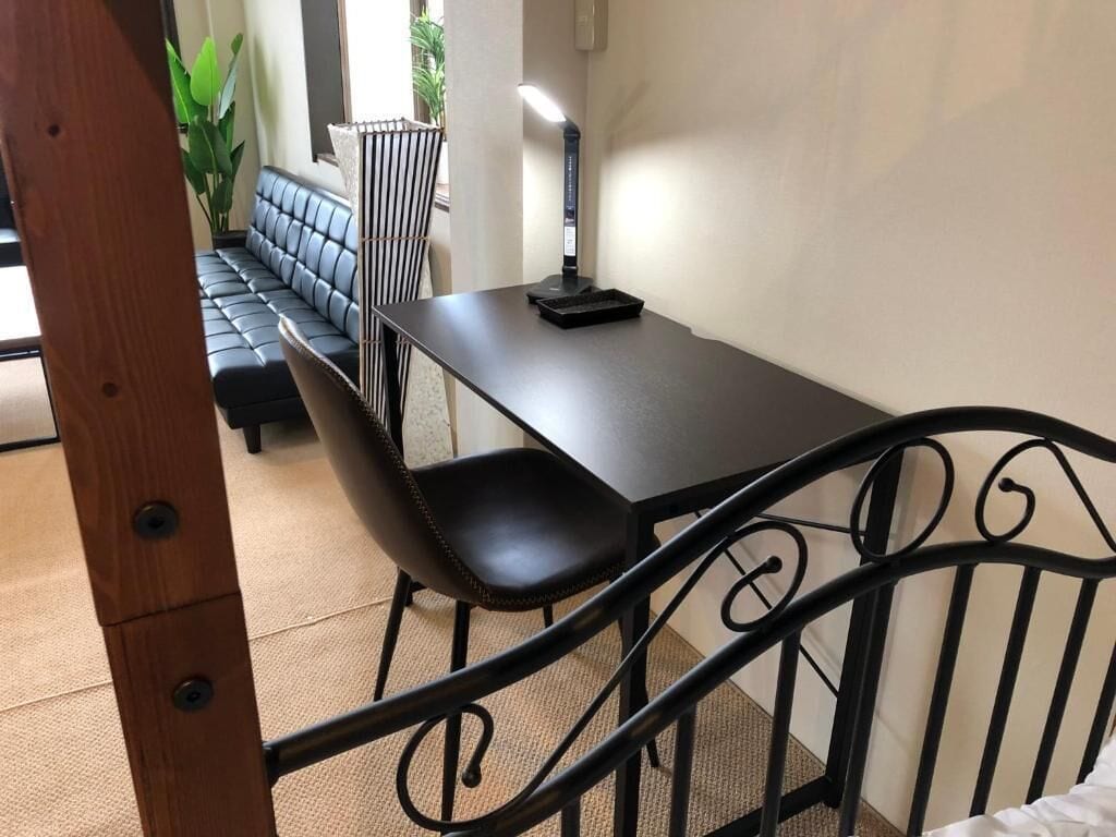 A room with a black metal bed frame, a wooden headboard, a black table with a lamp, and a black sofa.