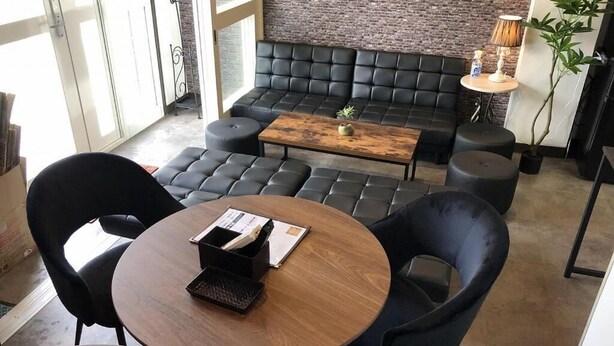 A modern lounge area with leather seating, a round wooden table, and a brick accent wall. - Cool-innOTARU (Otaru)