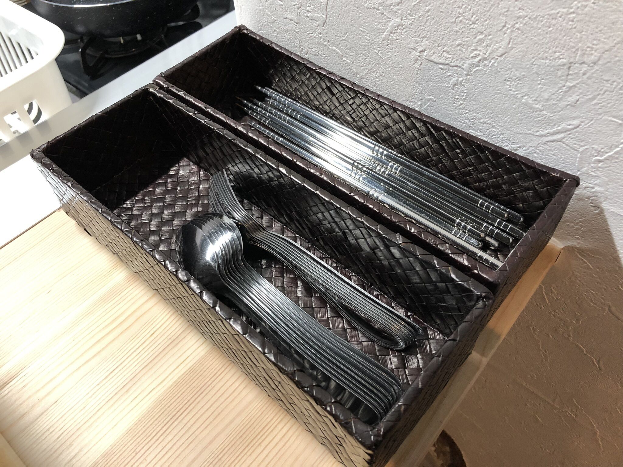 A kitchen with a black woven basket containing utensils and a white appliance in the background.
