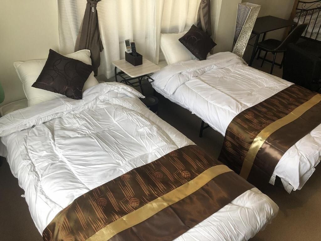 Two single beds with white and brown bedding, a small table with a remote control, and a chair.