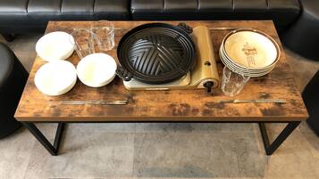 A dining table with a grill, plates, glasses, and chopsticks.