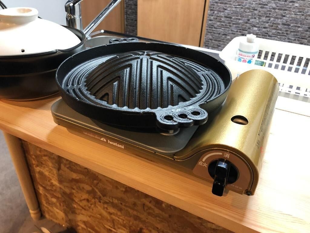 A kitchen with a waffle iron on a stove, a pot, and a bottle of milk.