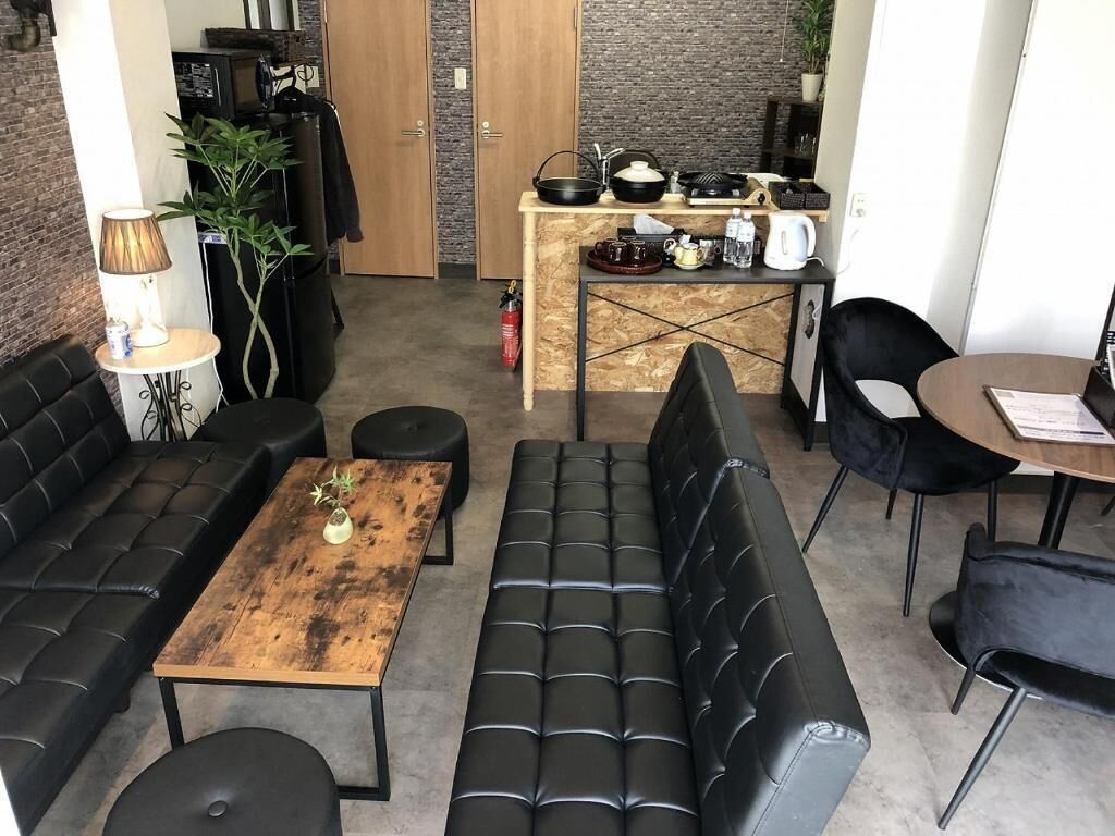 Uma sala de estar moderna com um sofá de couro preto, uma mesa de centro de madeira e um sofá de couro preto. Há uma área de cozinha com bancada e diversos utensílios.