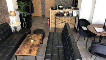 Una sala de estar moderna con un sofá de cuero negro, una mesa de centro de madera y un sofá cama de cuero negro. Hay una zona de cocina con una encimera y diversos utensilios.