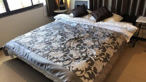 A neatly made bed with a patterned bedspread and pillows, a bedside table with a lamp, and a window with curtains. - Cool-innOTARU (Otaru)