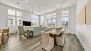 A spacious living room with a large wooden dining table, a sofa set, and a flat-screen TV.