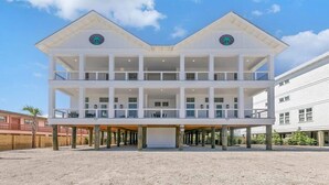 A two-story beachfront building with a covered lower level and a balcony on the upper level.