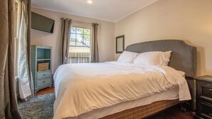 A bedroom with a large bed, a nightstand, a TV mounted on the wall, and a window with curtains.