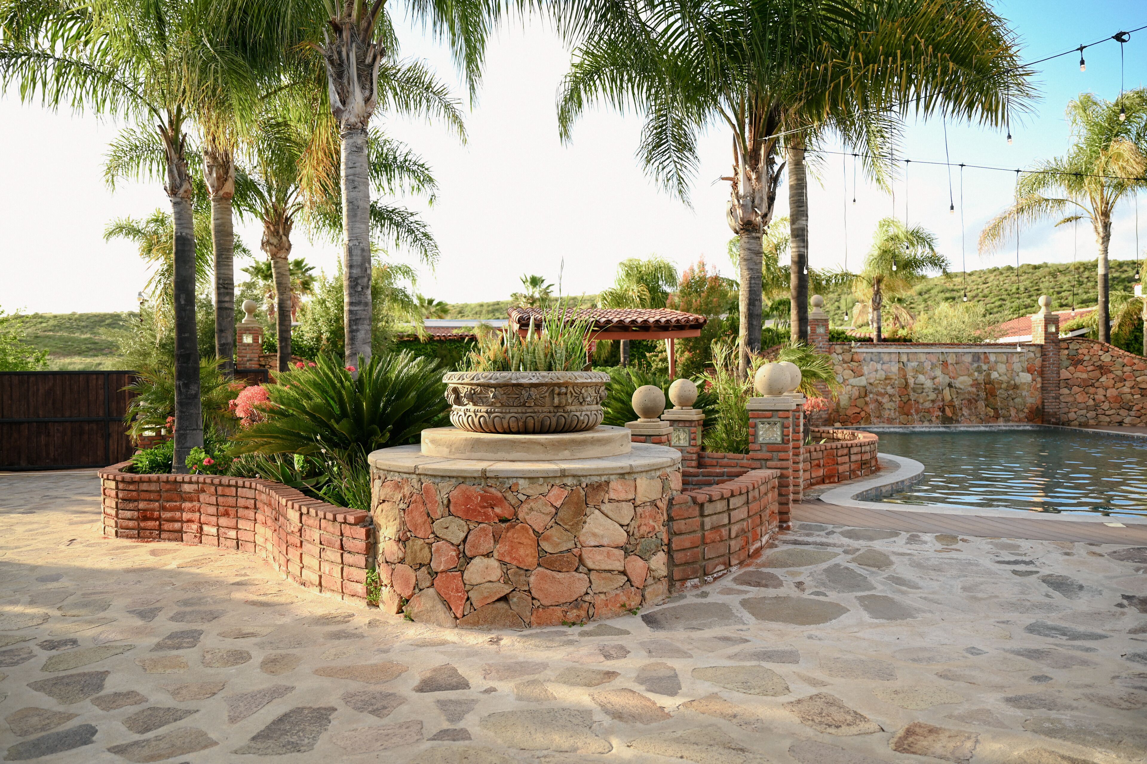 A stone patio with a pool, surrounded by palm trees and a stone wall.