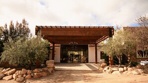 Een rustieke entree met een houten pergola, stenen muren en olijfbomen.