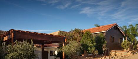 A two-story house with a red-tiled roof, a wooden pergola, and a stone wall.