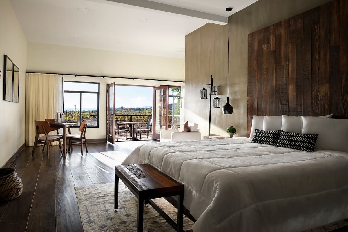 Een slaapkamer met een groot bed, een bureau en uitzicht op een wijngaard door de open deur.