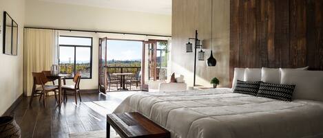 A bedroom with a large bed, a desk, and a view of a vineyard through the open door.