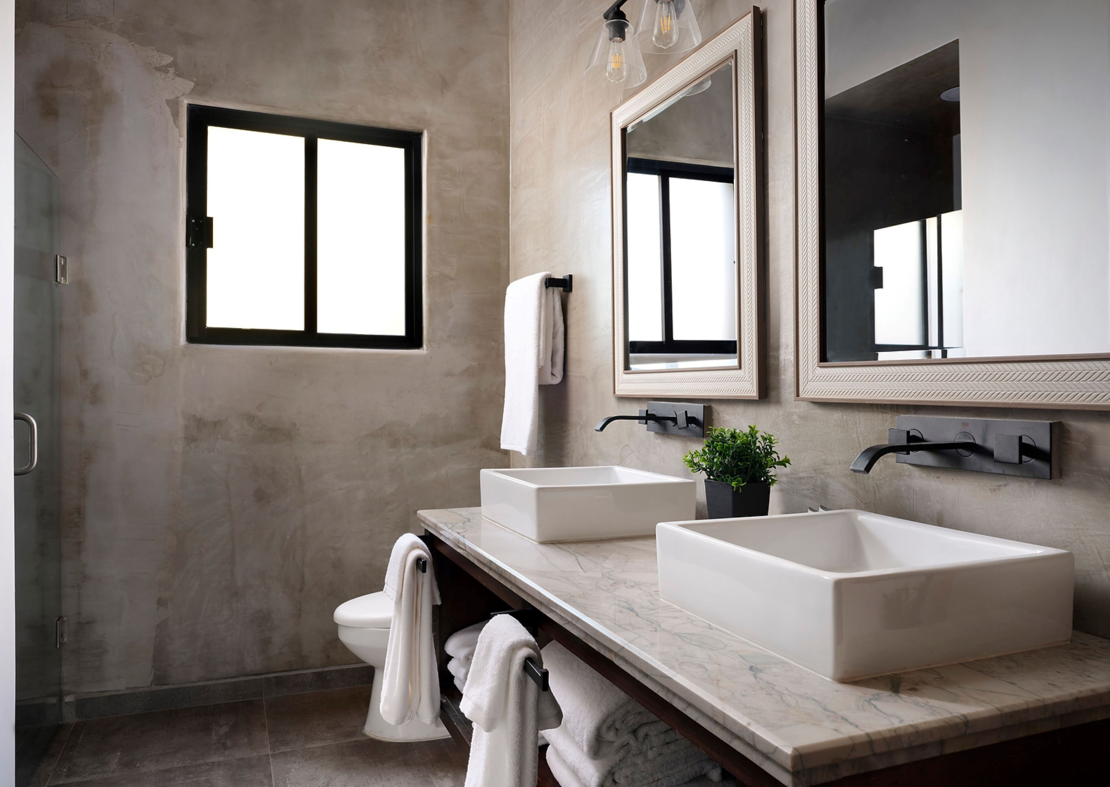 A modern bathroom with a large window, two sinks, a toilet, and a mirror.