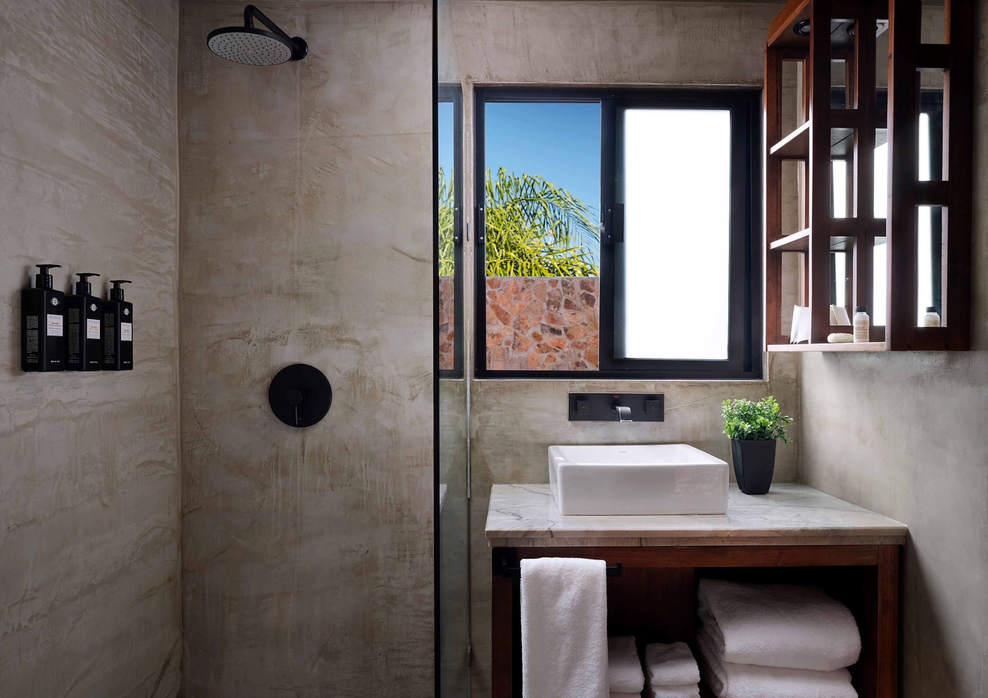 Une salle de bain moderne avec un grand miroir, une douche, un lavabo agrémenté d’une plante en pot et une fenêtre donnant sur un paysage verdoyant.