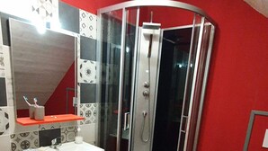 Een badkamer met een rode wand, een douchecabine van glas, een wit wastafelmeubel in rood, en een wit toilet.