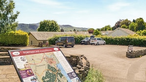 A parking area with a map sign, a stone wall, and vehicles. - Peaceful village location within walking distance to Keswick. (Portinscale, Keswick)