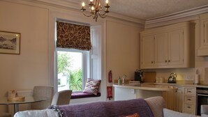 A living room with a sofa, a glass coffee table, and a window with a view of greenery outside. - Peaceful village location within walking distance to Keswick. (Portinscale, Keswick)
