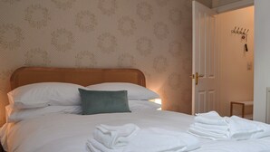 A neatly made bed with white linens and a green pillow, a folded white towel on the bed, and a door with a coat rack in the background. - Peaceful village location within walking distance to Keswick. (Portinscale, Keswick)