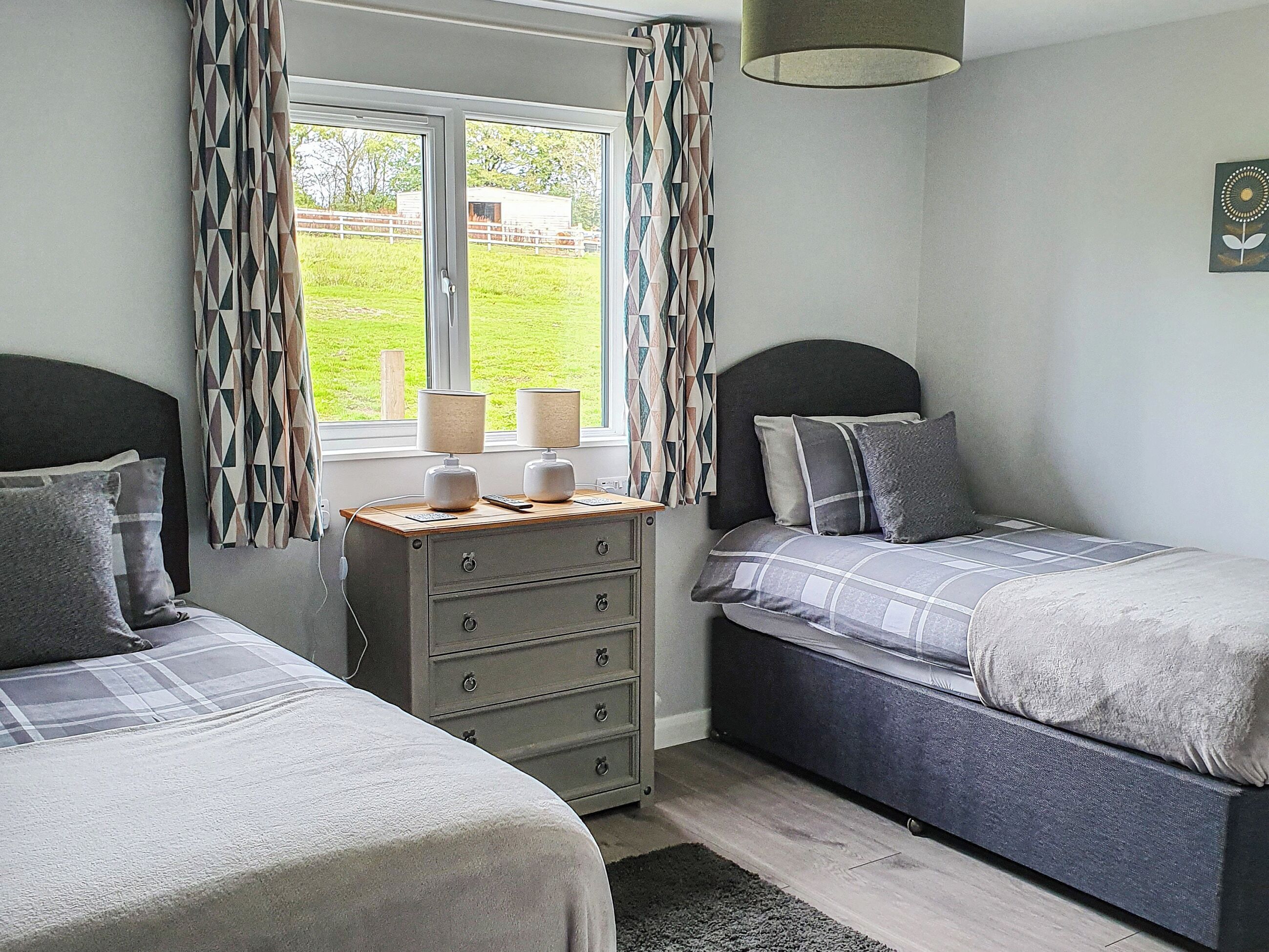 A bedroom with two beds, a dresser, and a window with curtains.