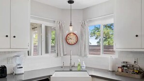 A modern kitchen with white cabinets, a built-in dishwasher, a large window with curtains, and a wall clock. - Close to Downtown! Gorgeous MidCentury w/fire pit (Paso Robles)