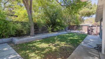 A backyard with a grassy lawn, a tree, a brick wall, and a concrete pathway.