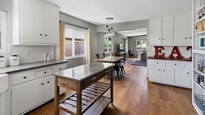 A modern kitchen with white cabinets, a wooden island, and a dining area in the background. - Close to Downtown! Gorgeous MidCentury w/fire pit (Paso Robles)