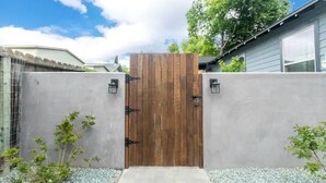 A wooden gate with a concrete wall, a small pathway, and a tree. - Lovely Remodeled Home! Walk Downtown! w/firepit (Paso Robles)