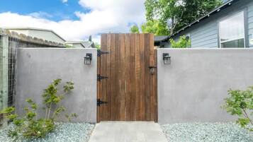 Una verja de madera con un muro de concreto, un pequeño sendero y un árbol.