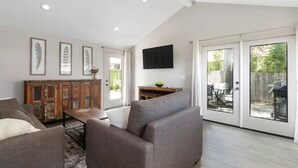 A spacious living room with a sofa, a coffee table, and a cabinet. There is a sliding glass door leading to an outdoor area. - Lovely Remodeled Home! Walk Downtown! w/firepit (Paso Robles)