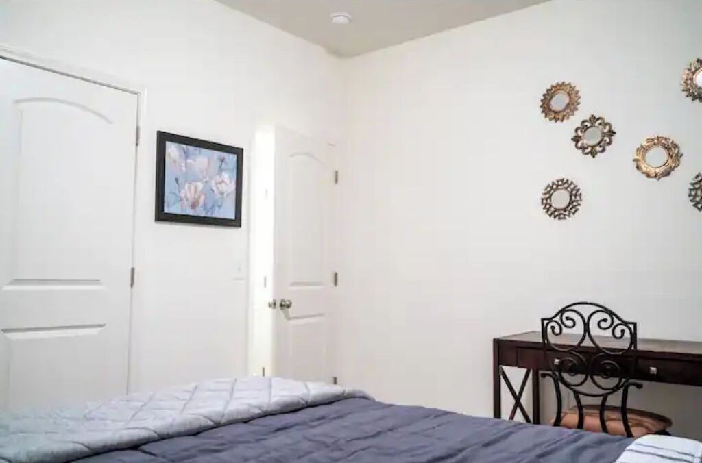 Een slaapkamer met een bed, een bureau en een stoel. Er zijn decoratieve spiegels aan de muur en een ingelijste foto.