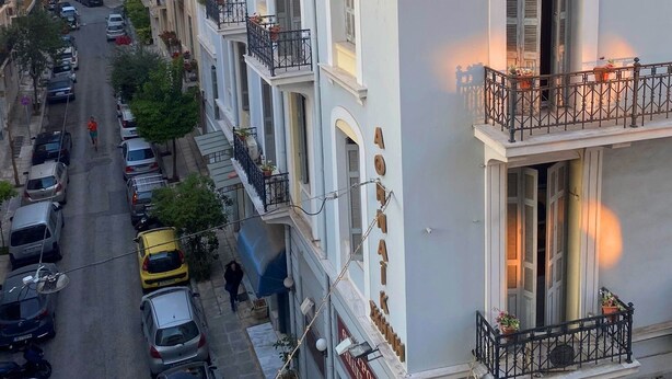 Une rangée de bâtiments blancs dotés de balcons, des voitures garées et une rue dégagée.