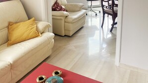 Un salon avec un canapé beige, une table basse rouge et un coin repas comprenant une table et des chaises.