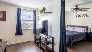 A bedroom with a bed, a TV on a stand, a ceiling fan, and a window with curtains. - 1 BR with Ocean View - unit 1 (Fort Myers Beach)