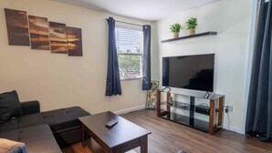 A living room with a sofa, a coffee table, a TV on a stand, and artwork on the wall. - 1 BR with Ocean View - unit 1 (Fort Myers Beach)