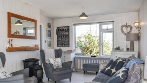 Tunnelmallinen olohuone, jossa on takka, mukavat istuimet, suuri peili ja ikkuna, josta avautuu näkymä vehreään maisemaan.
