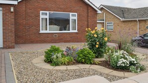 A two-story brick house with a large window and a garden with various plants and flowers. - Hollins on the Coast (Bridlington)