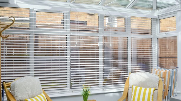 A sunroom with large windows, two wooden chairs with cushions, a small table, and a radiator. - Hollins on the Coast (Bridlington)