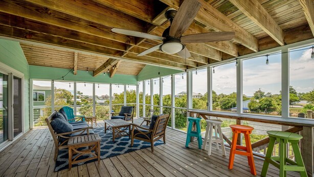 Eine überdachte Terrasse im Freien mit Holzmöbeln, einem Deckenventilator und großen Fenstern mit Blick ins Grün.