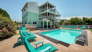 Ein Poolbereich mit einem türkisblauen Pool, einem mehrstöckigen Gebäude inklusive Rutsche und mehreren türkis-farbenen Liegestühlen.